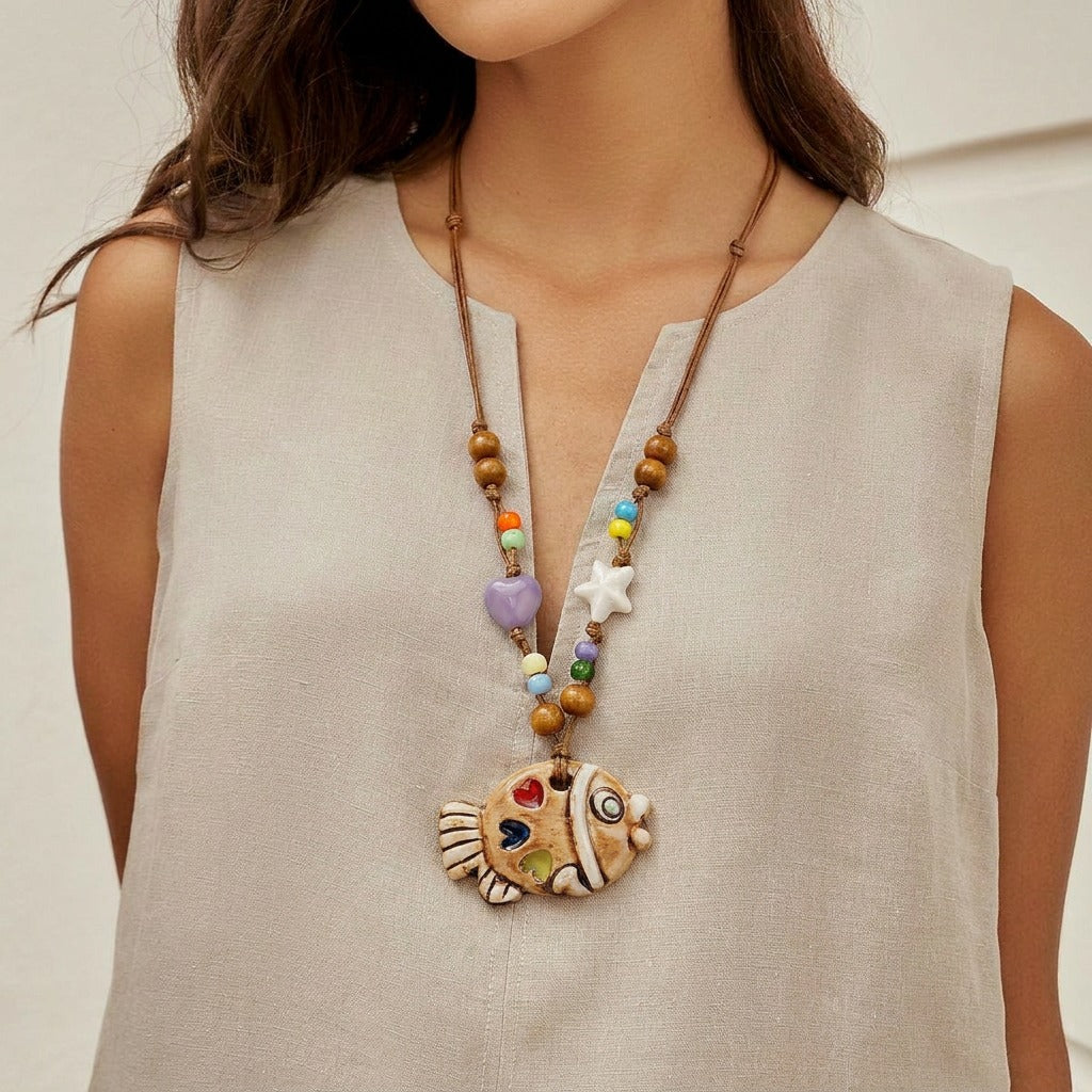 A playful blend of color and craftsmanship, this handmade fish pendant carries tiny heart details that feel full of warmth and personality. With its artistic ceramic finish and soft earthy tones, it brings a whimsical, story-like charm to your everyday look.