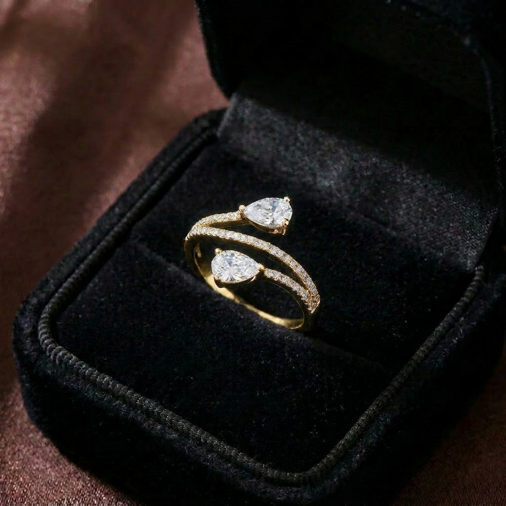 A graceful dance of symmetry and sparkle, this ring features two radiant pear-cut stones flowing toward each other in an elegant open-wrap silhouette. The curved pavé band creates a soft, modern brilliance that feels refined and effortlessly romantic.