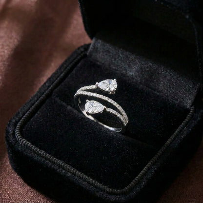 A graceful dance of symmetry and sparkle, this ring features two radiant pear-cut stones flowing toward each other in an elegant open-wrap silhouette. The curved pavé band creates a soft, modern brilliance that feels refined and effortlessly romantic.
