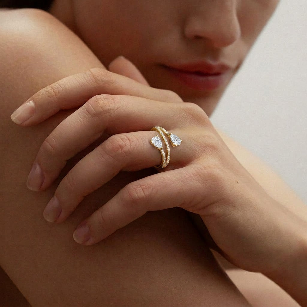 A graceful dance of symmetry and sparkle, this ring features two radiant pear-cut stones flowing toward each other in an elegant open-wrap silhouette. The curved pavé band creates a soft, modern brilliance that feels refined and effortlessly romantic.