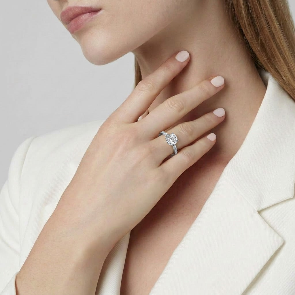A graceful brilliance wrapped in timeless elegance, this ring features a radiant round-cut centerpiece embraced by a delicately curved pavé band. Its soft sparkle and refined silhouette create a look that feels romantic, luxurious, and effortlessly classic.